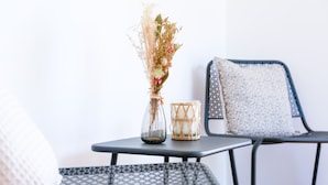 A small table with a vase of dried flowers and a candle, and two chairs with patterned cushions.