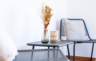 Une petite table ornée d’un vase de fleurs séchées et d’une bougie, ainsi que deux chaises avec des coussins à motifs.