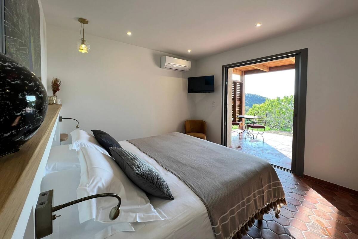 Un dormitorio con cama, una silla, un televisor y vistas al exterior.