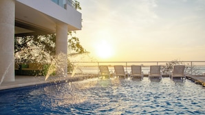 Une piscine dotée de jets d’eau, de chaises longues et offrant une vue sur le coucher de soleil.