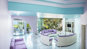 Un salon moderne avec un canapé blanc aux lignes courbes, un plus petit canapé violet et une table basse en verre.