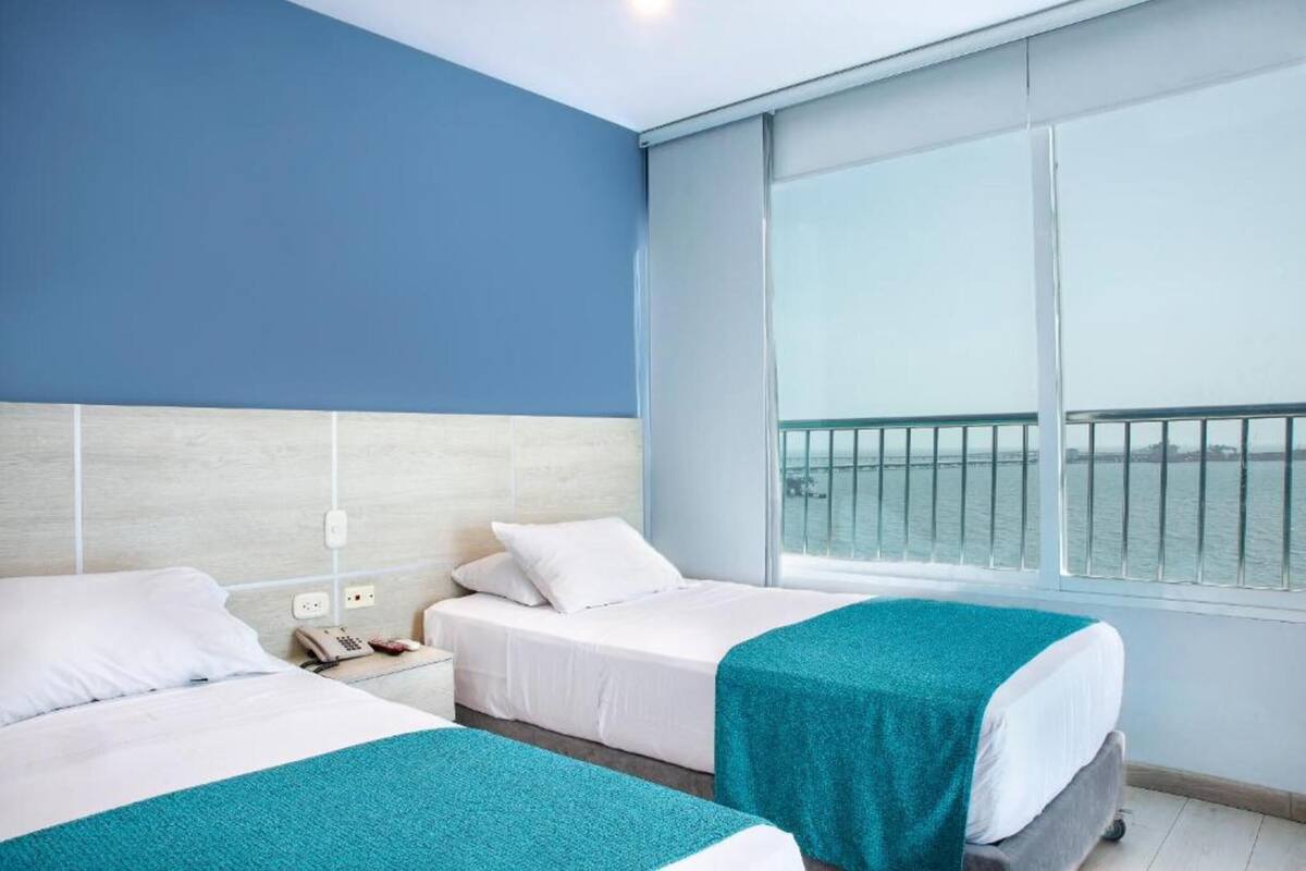 Une chambre d’hôtel avec deux lits, une grande fenêtre donnant sur la mer et un balcon.