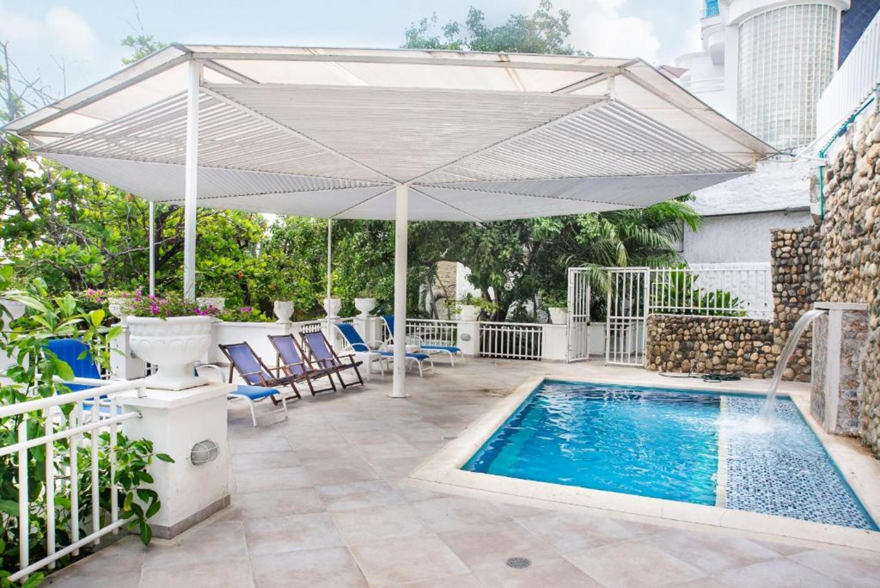 A pool area with a covered seating area, lounge chairs, and a stone wall.
