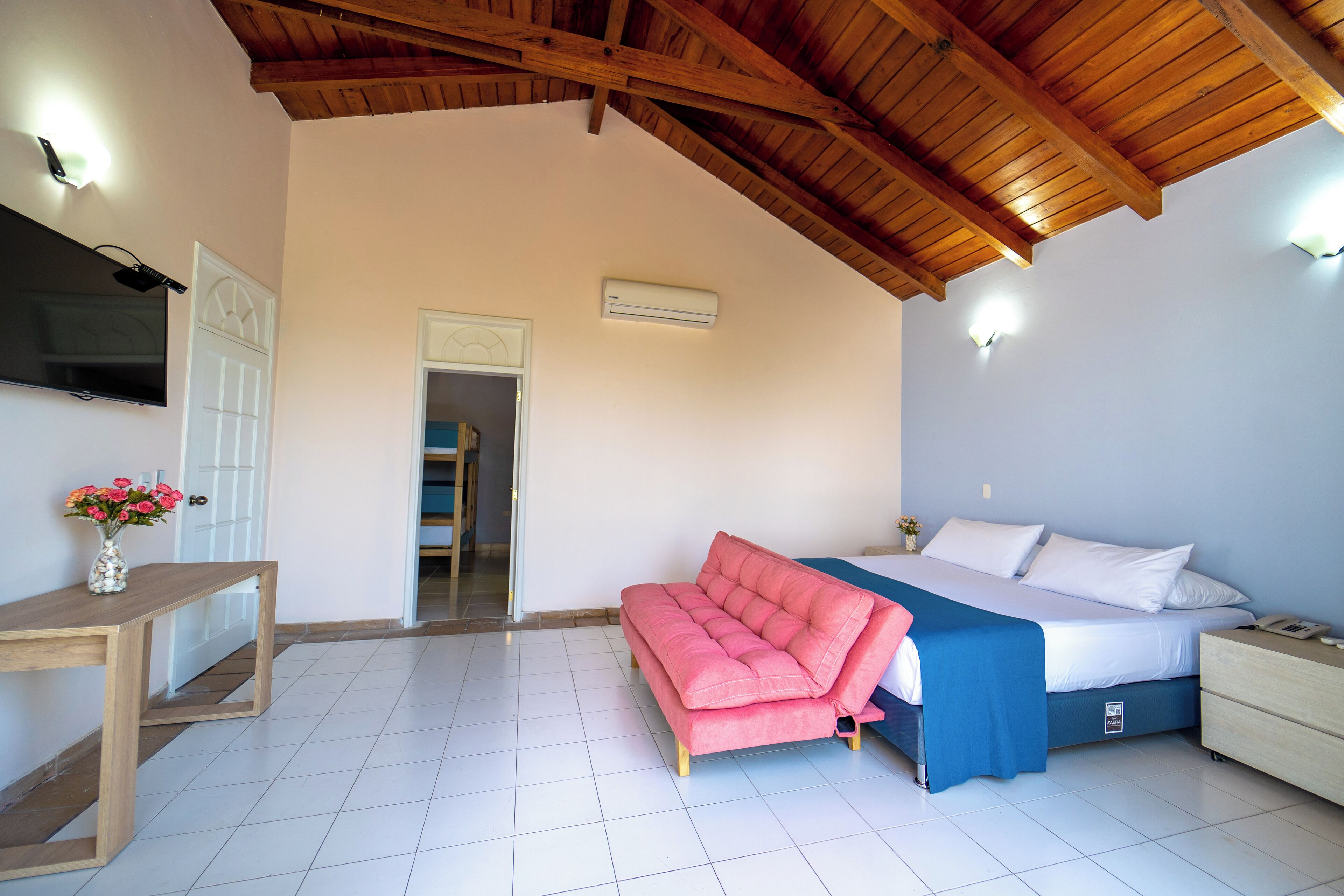 A bedroom with a bed, bedside table, and a pink sofa.