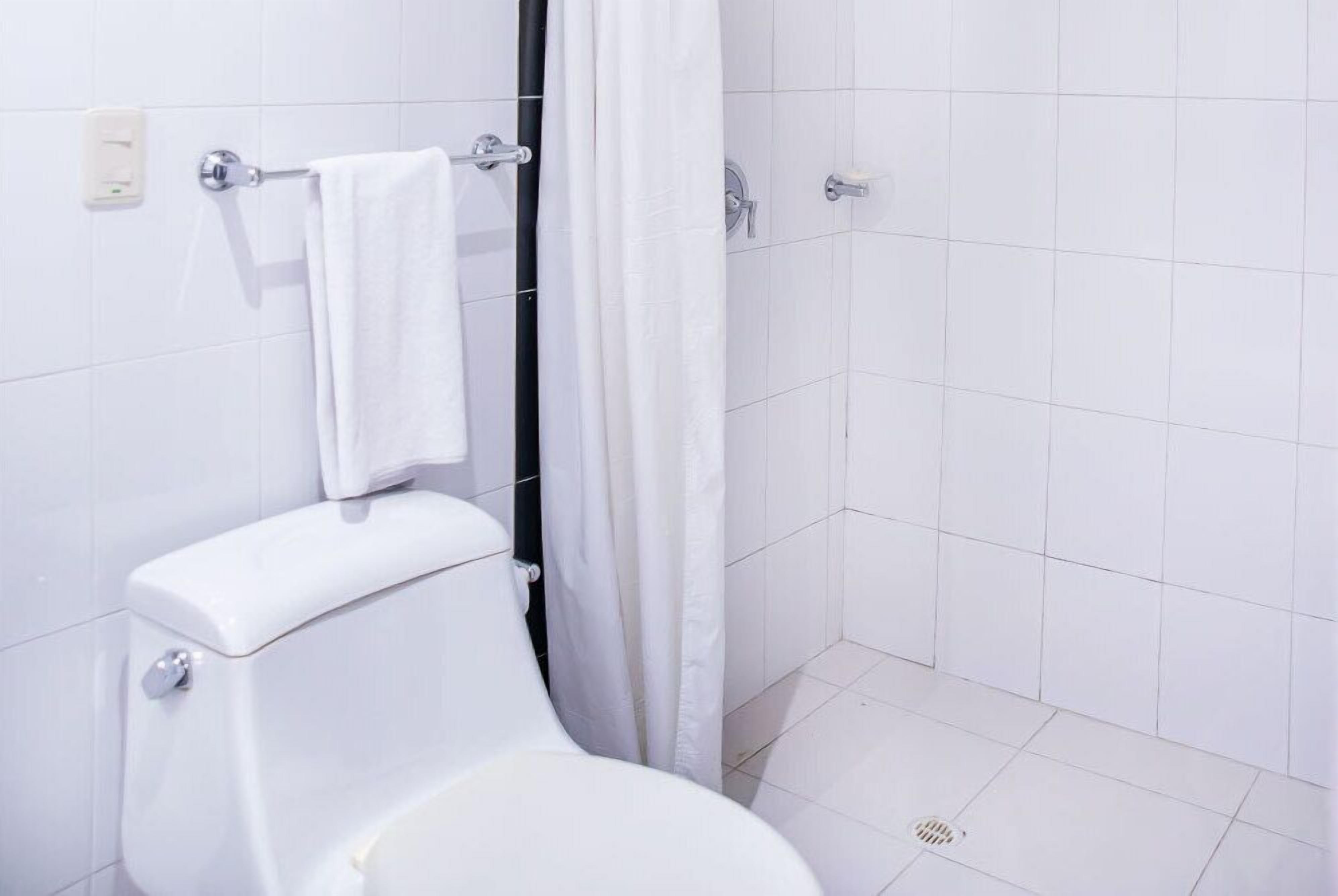 Un baño con un inodoro blanco, una toalla colgada en un perchero y una cortina de ducha.