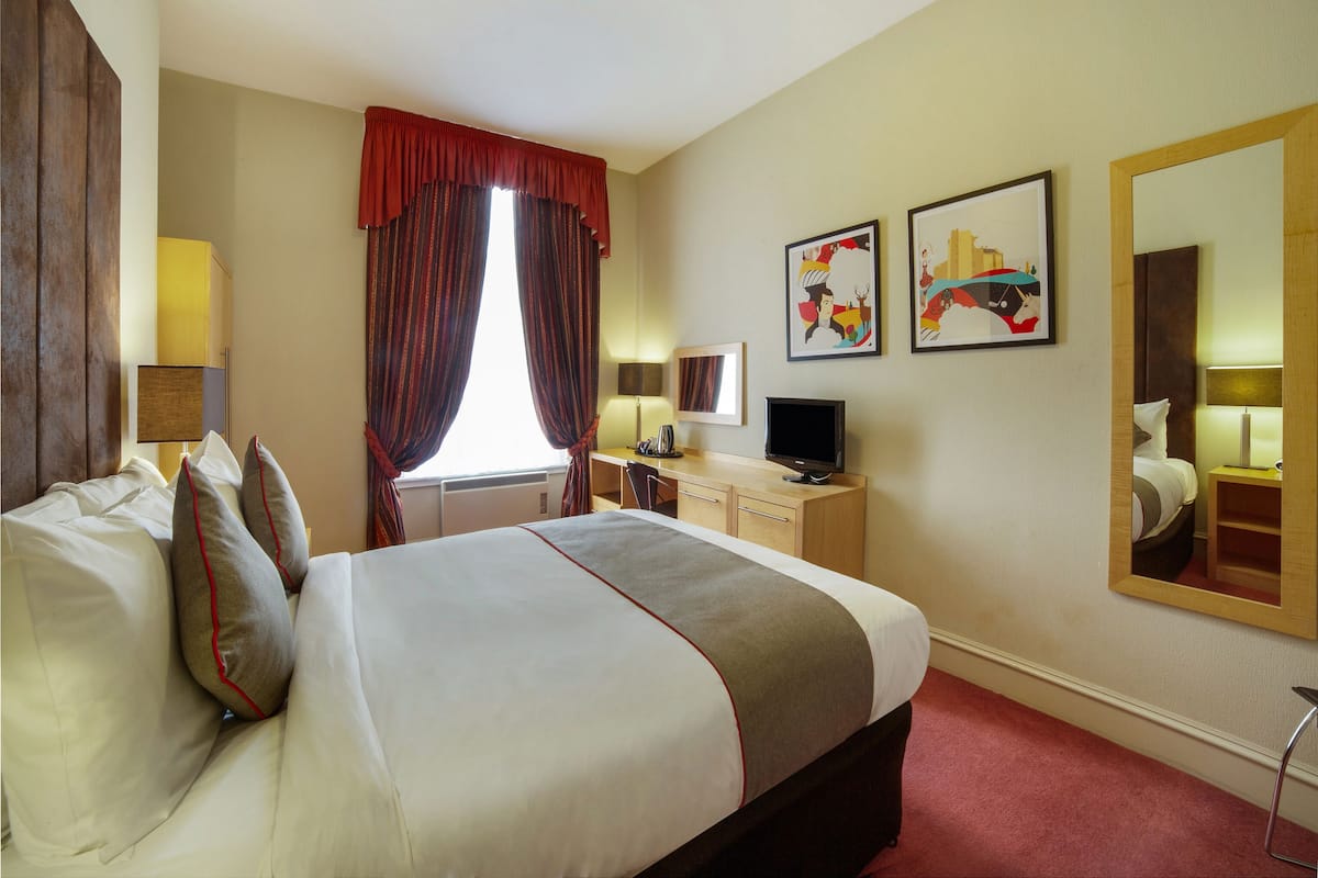 Una habitación de hotel con una cama, un escritorio, un televisor y obras de arte en la pared.