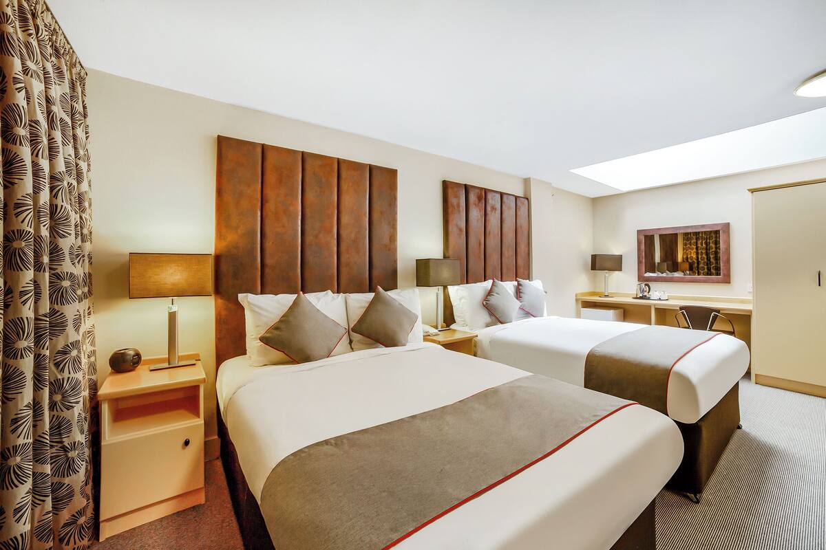 Une chambre d’hôtel avec deux lits, un bureau, une chaise, une table de chevet et un miroir.