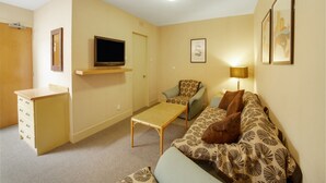 A compact living space with a television, a sofa, a chair, a small table, and a desk with drawers.