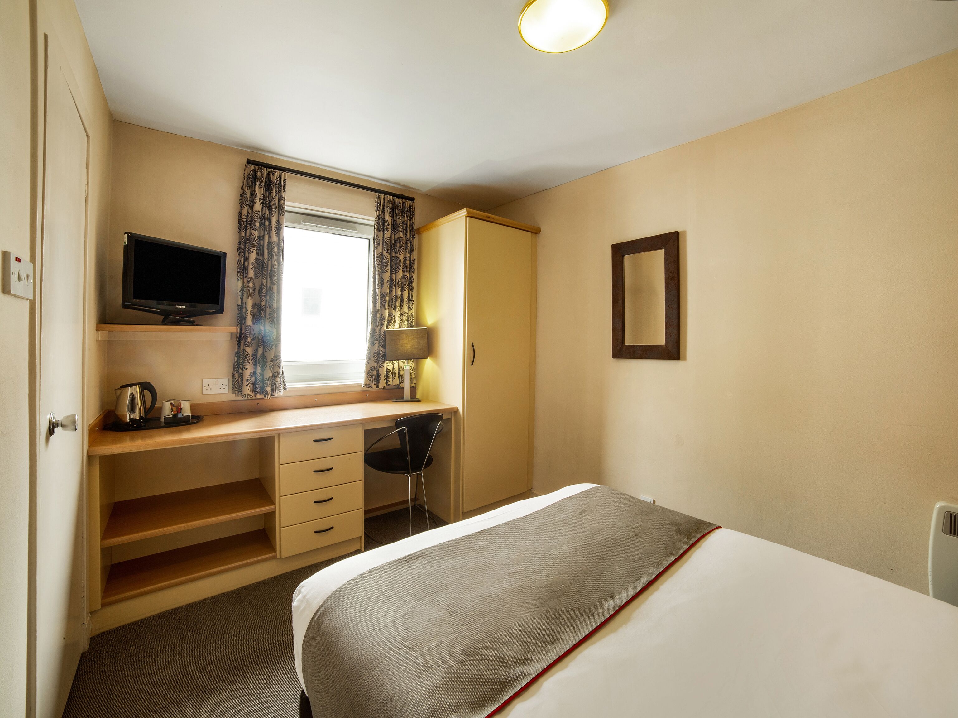 Habitación de hotel con cama, escritorio con silla, televisor y ventana con cortinas.