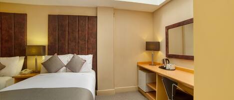 A hotel room with a bed, bedside table, lamp, desk, chair, and a mirror.