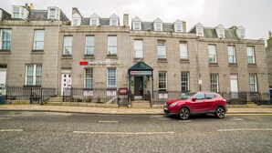 A multi-story hotel with a traditional stone facade, a prominent entrance, and a red car parked in front.