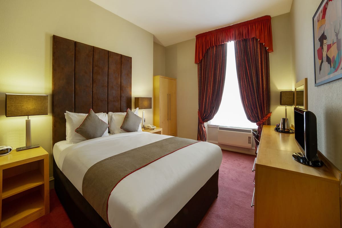 Habitación de hotel con una cama grande, un escritorio con computadora, un armario y una ventana con cortinas.