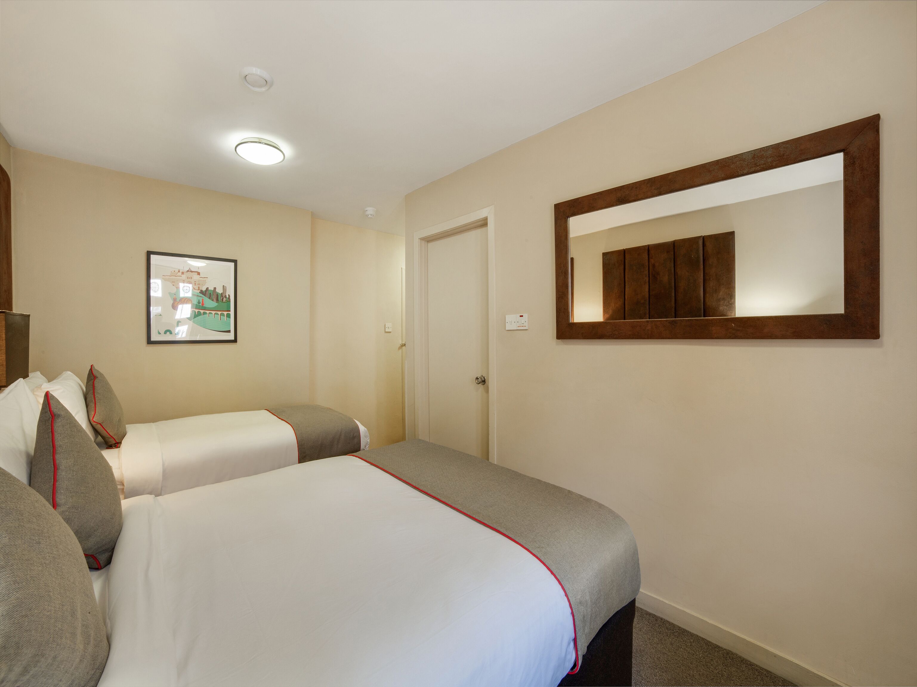 Ein Hotelzimmer mit zwei Betten, einem gerahmten Bild an der Wand, einem Spiegel und einer Tür.