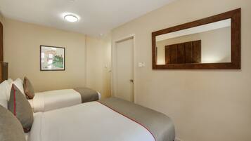 A hotel room with two beds, a framed picture on the wall, a mirror, and a door.