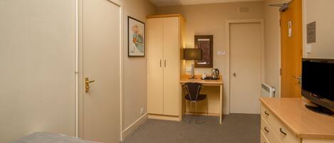 Une chambre d’hôtel avec deux lits simples, un bureau avec une chaise, une télévision, un petit coin cuisine et une porte donnant sur une autre chambre.