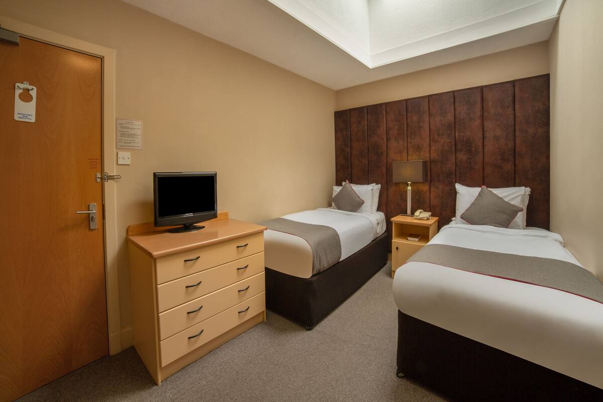 Habitación de hotel con dos camas, un televisor en una cómoda, un escritorio con lámpara y un tragaluz en el techo.