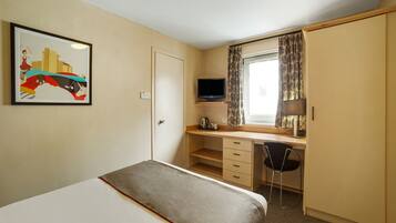 A hotel room with a bed, a desk with a chair, a television, and a window with curtains.