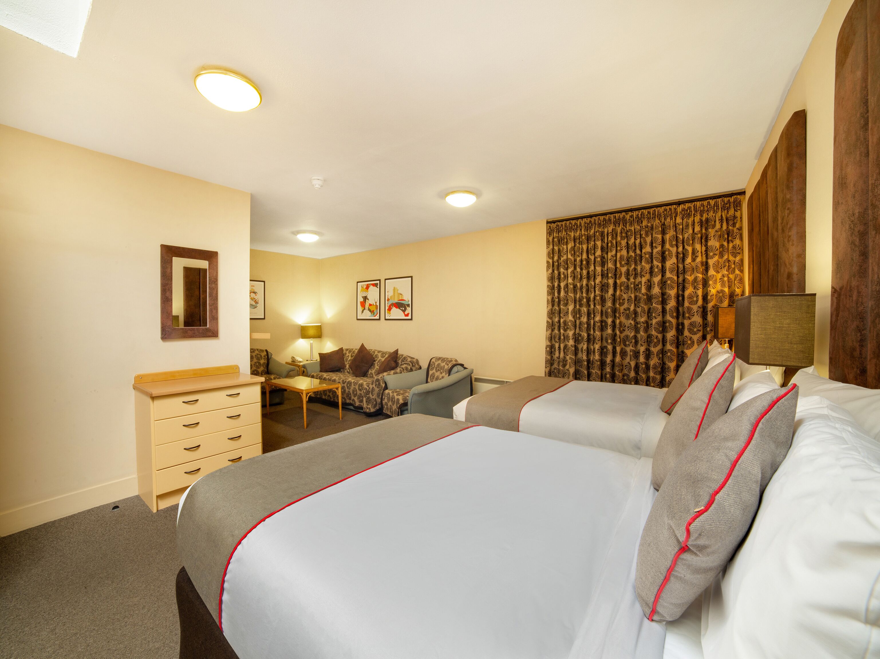 A hotel room with two beds, a sofa, a small table, and a dresser.