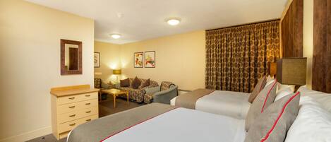 A hotel room with two beds, a sofa, a small table, and a dresser.