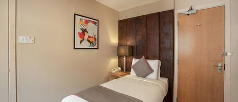 Une chambre d’hôtel avec un lit, une table de chevet avec une lampe, une porte et un interrupteur fixé au mur.