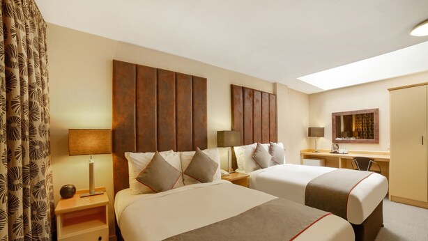 A hotel room with two beds, a desk, a chair, a mirror, and a window.