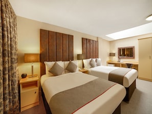 Habitación de hotel con dos camas, un escritorio, una silla, un espejo y una ventana.