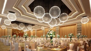 Een balzaal met ronde tafels gedekt voor diner, grote kristallen kroonluchters en bloemstukken als decoratie.