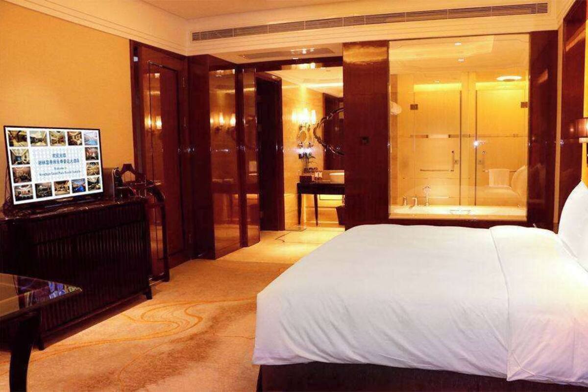 A hotel room with a large bed, a television, a desk, and a bathroom with a shower and toilet.