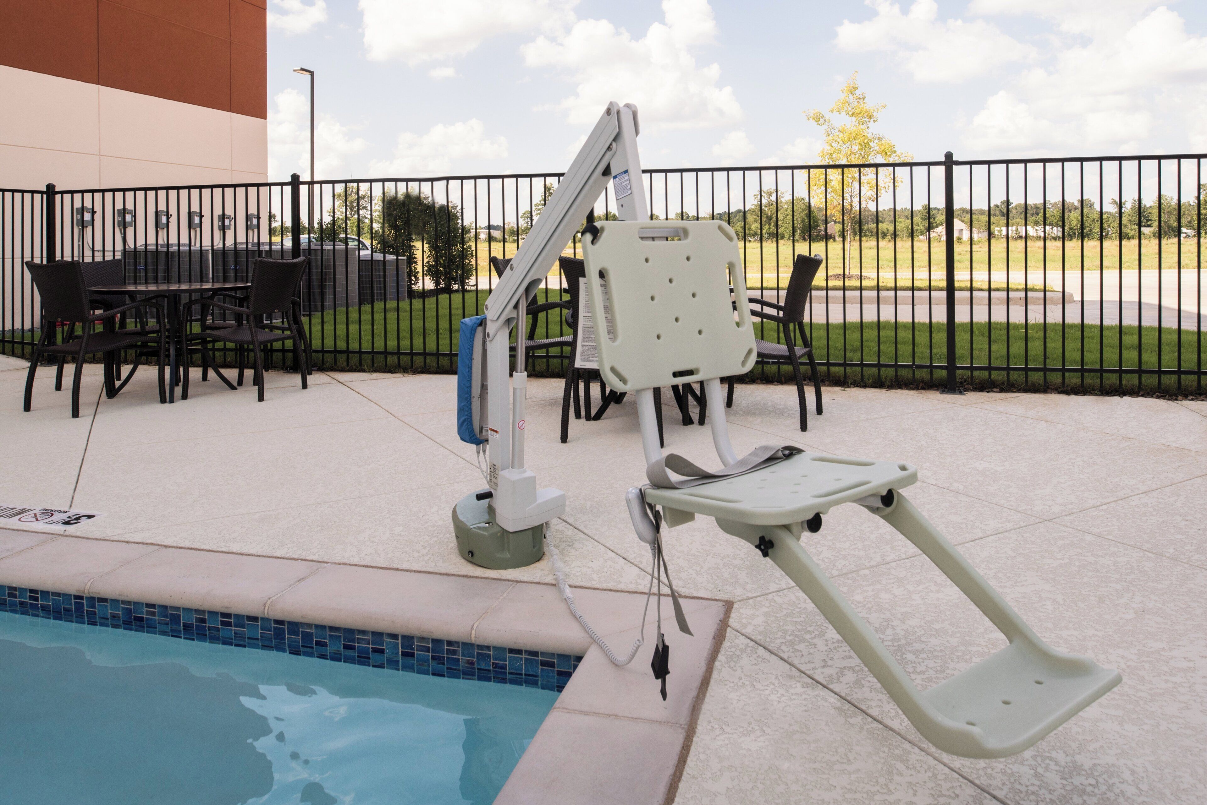 Uma área à beira da piscina com elevador para piscina acessível em cadeira de rodas, assentos externos e piscina cercada.