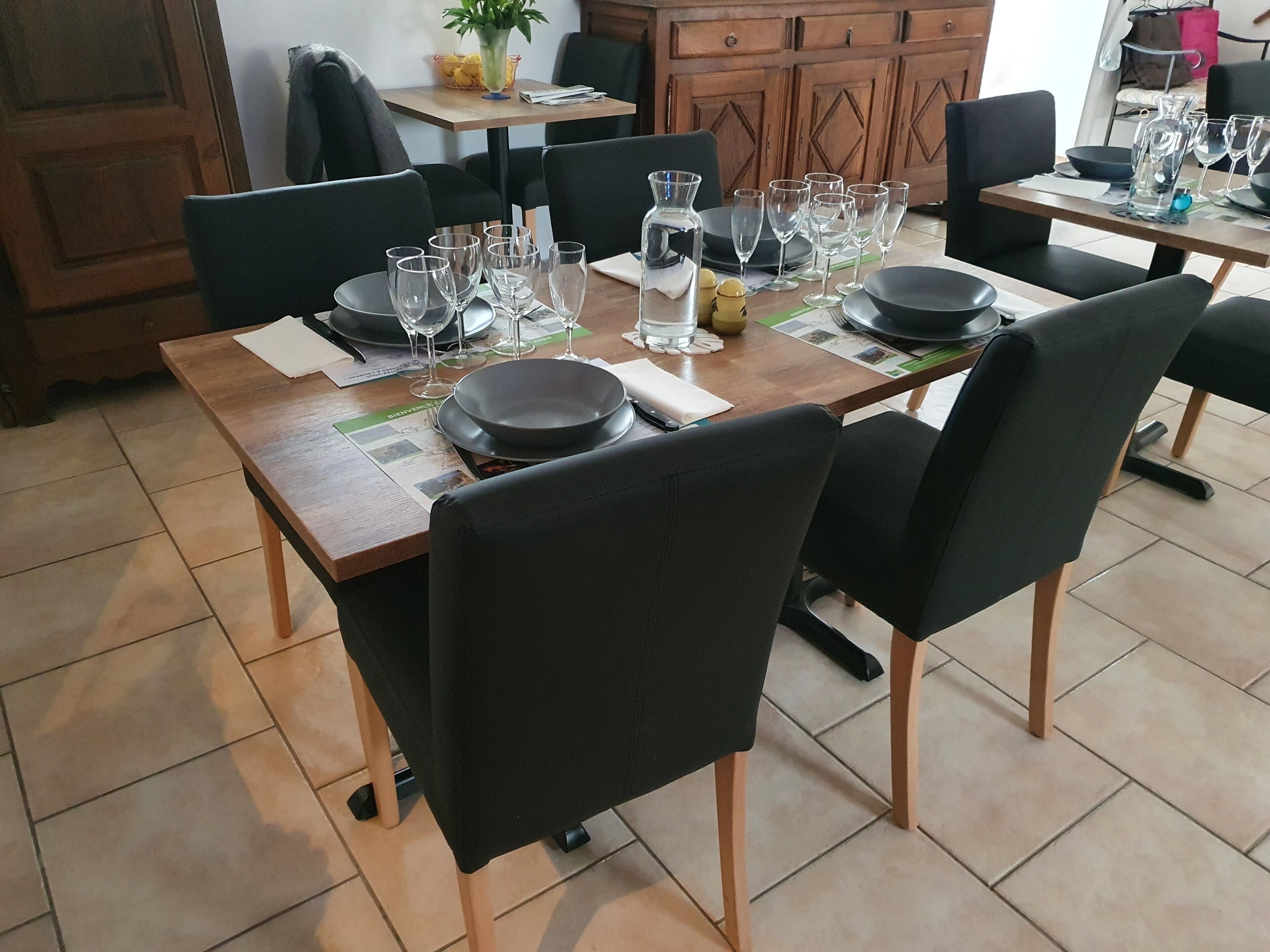 A dining area with a wooden table set for four, black chairs, and a variety of glassware and plates.