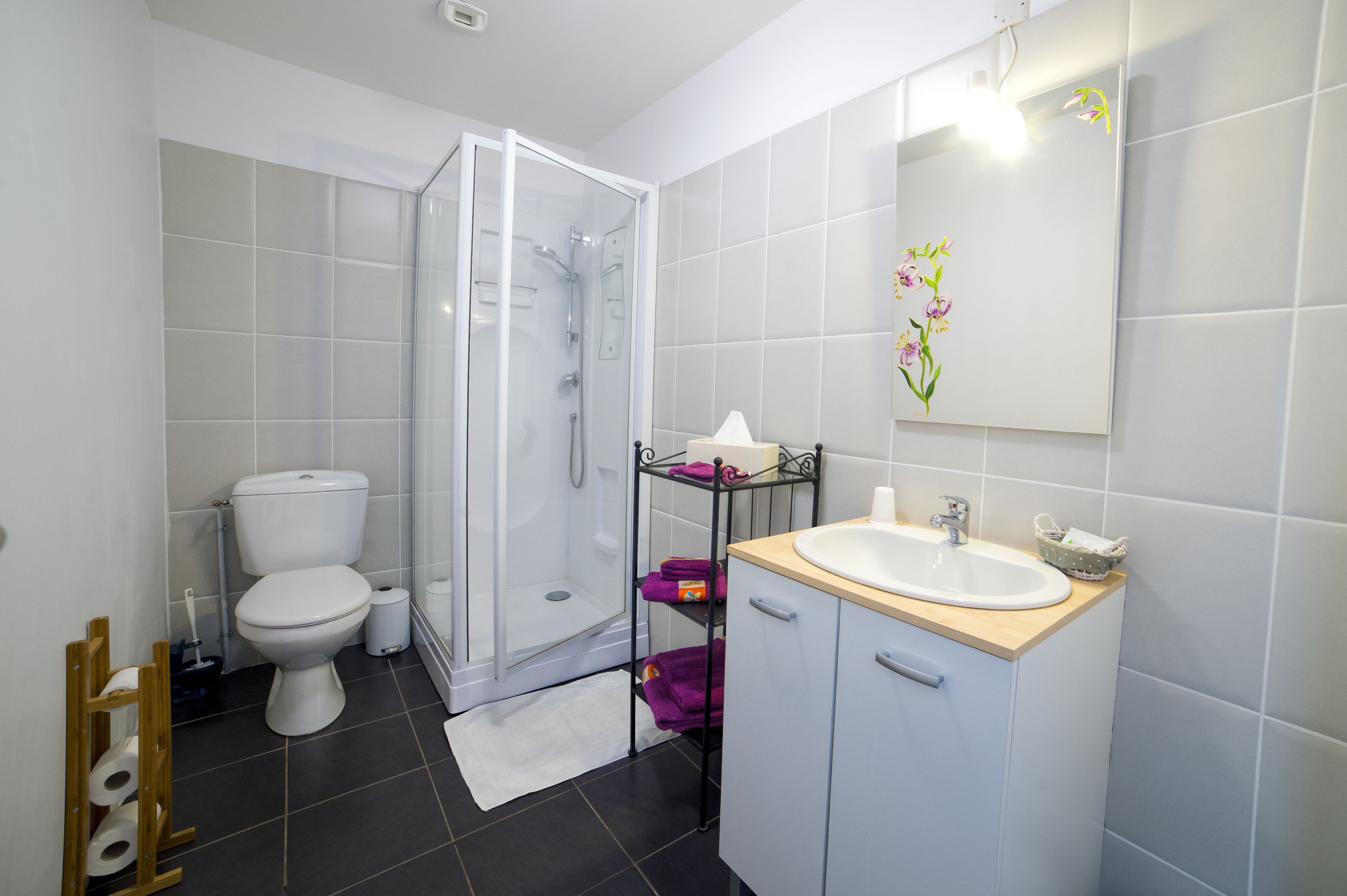 Une salle de bain équipée de toilettes, d’une douche, d’un lavabo et d’une étagère où sont rangées les serviettes.