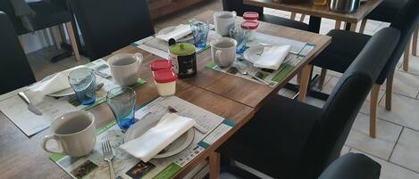 A dining area with wooden tables, black chairs, and a variety of tableware including plates, cups, and cutlery.
