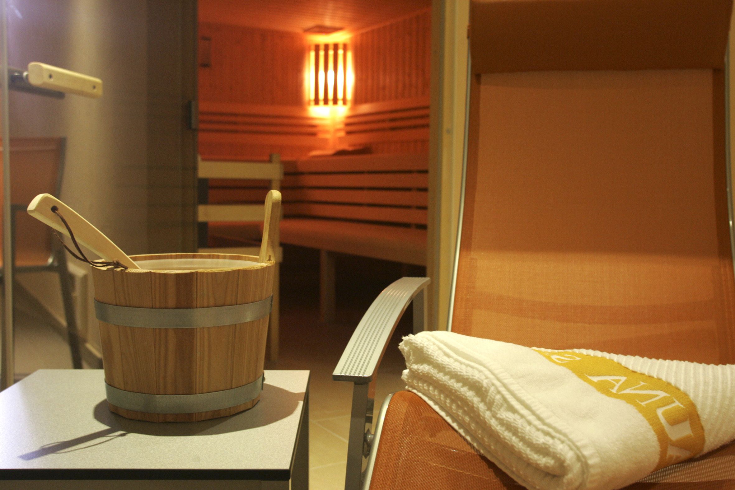 A sauna room with a wooden bucket, a towel with a logo, and a bench.