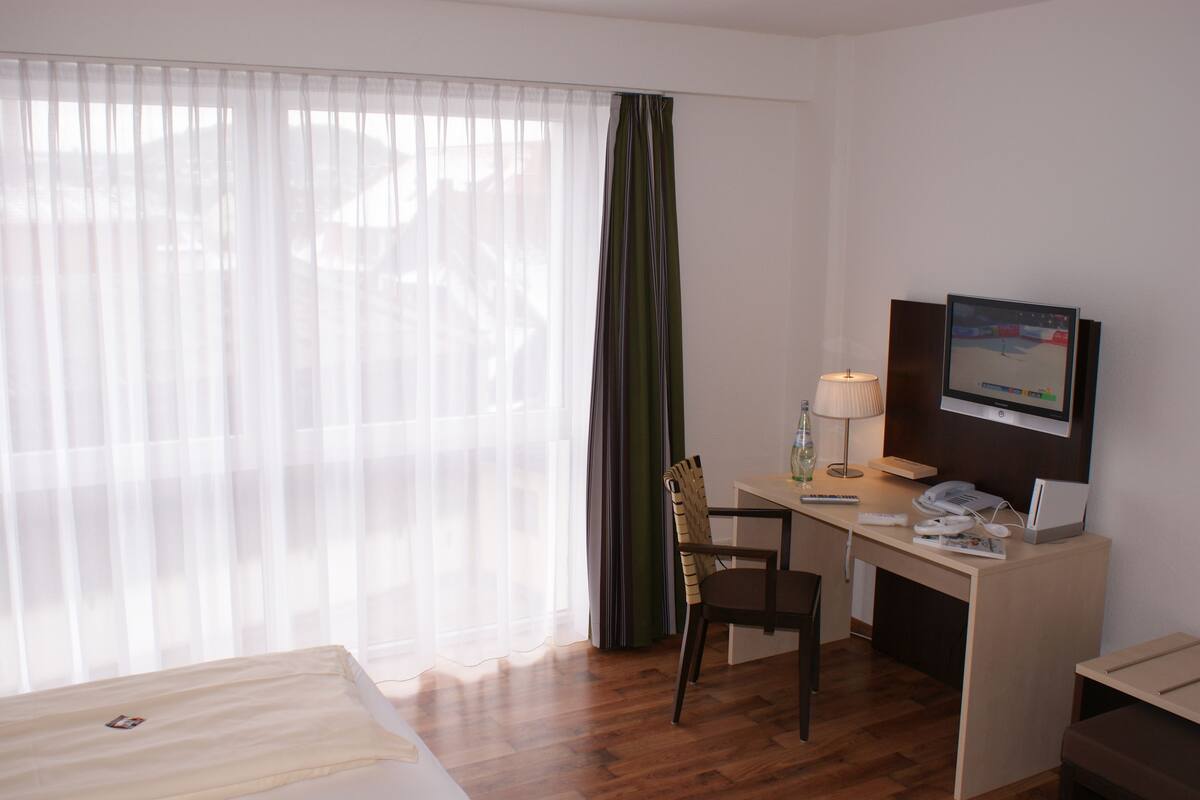A hotel room with a bed, a desk with a computer, a chair, a lamp, and a television.