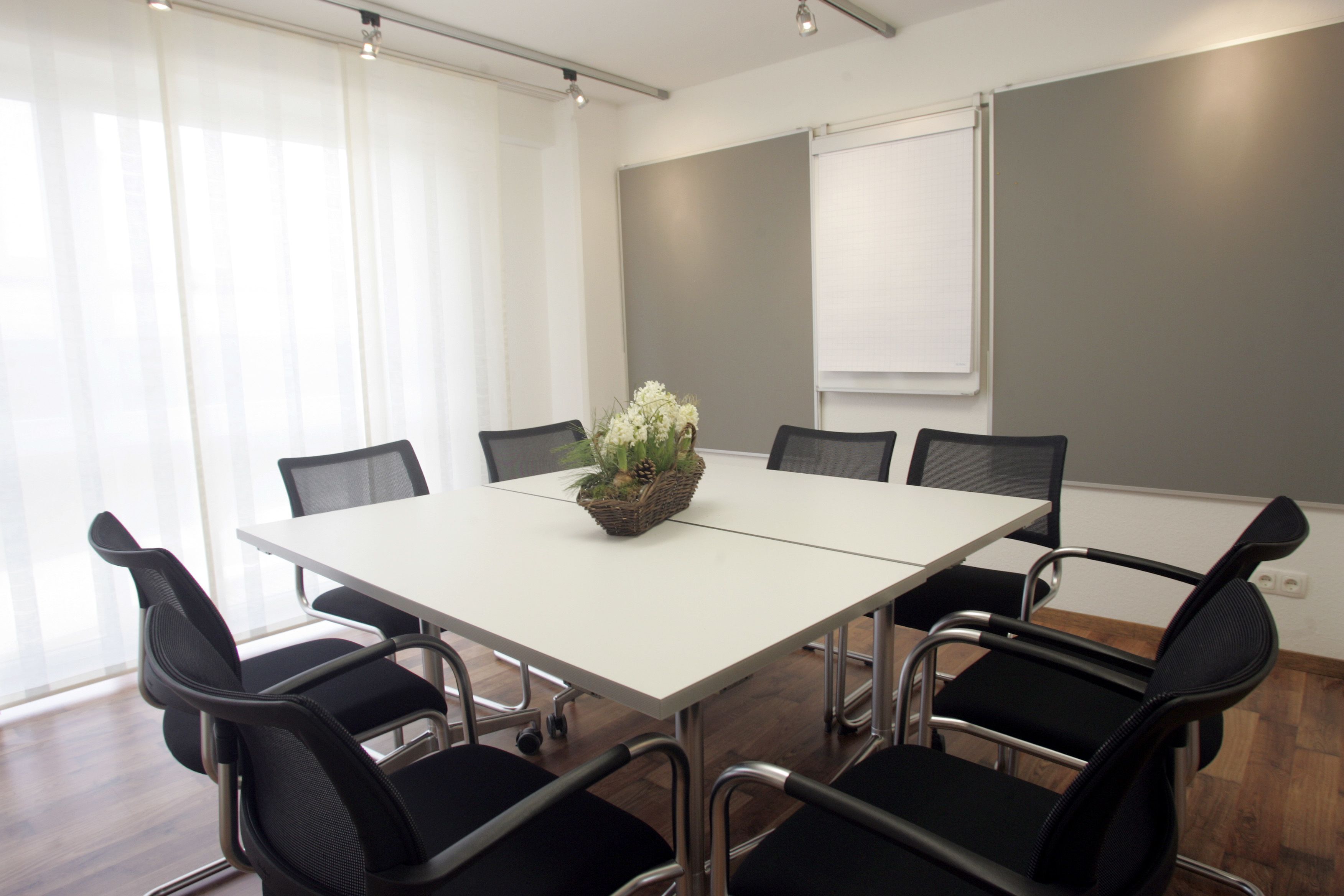 Un salón de conferencias con una mesa blanca, seis sillas negras y un centro de mesa con planta decorativa.