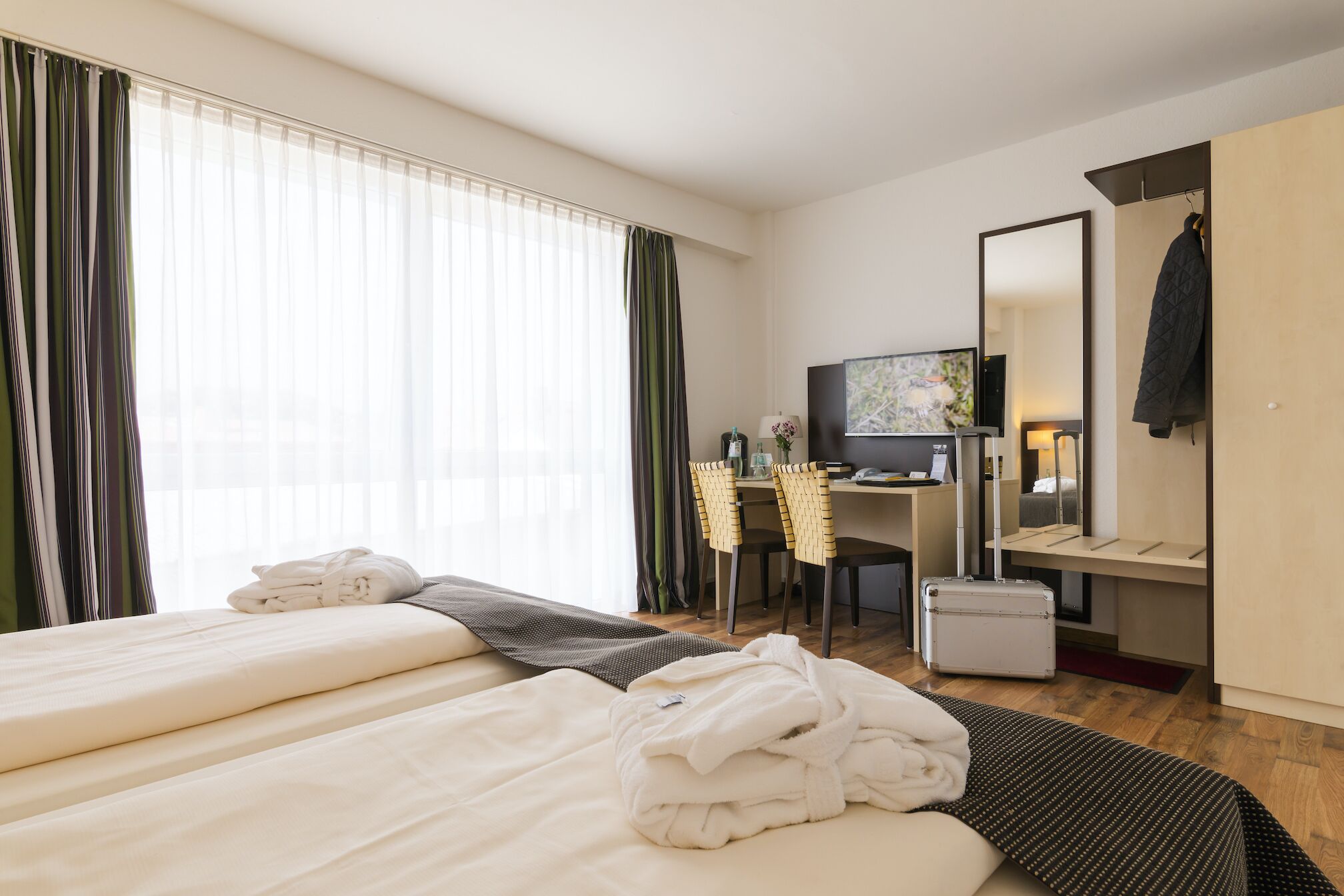A hotel room with two beds, a desk with a computer, a TV, and a mirror.