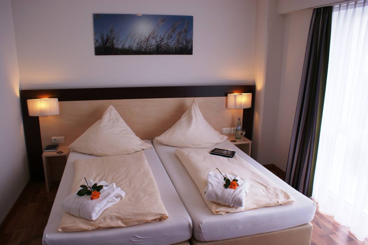 A hotel room with two beds, each with a pillow, a bedside lamp, and a small table with a phone and a bottle.