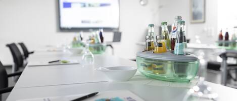 A conference room with a long table, a projector screen, and a glass bowl with bottles.