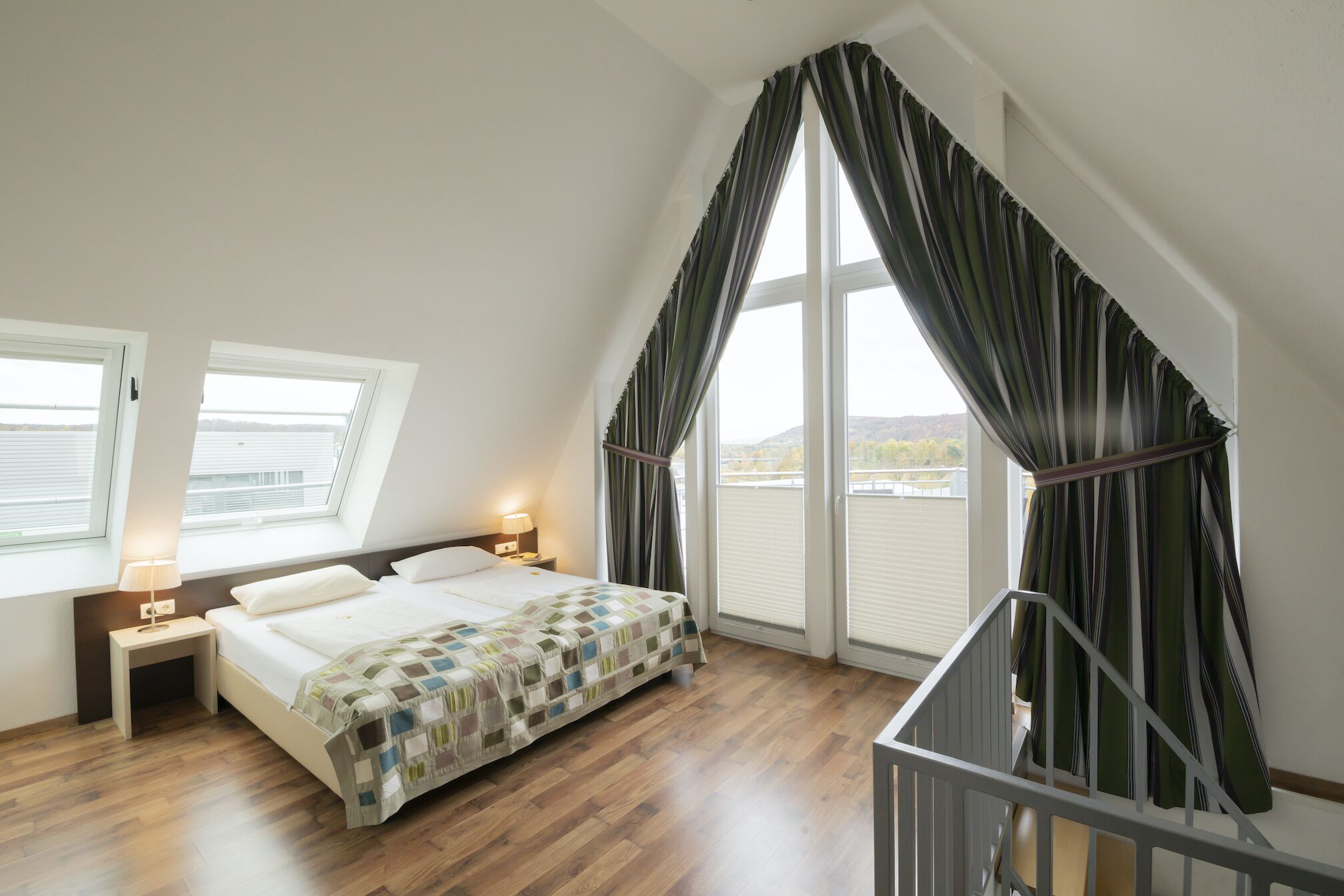 Un dormitorio con cama, dos mesitas de noche, una lámpara auxiliar y una ventana con persianas, con vistas al exterior.