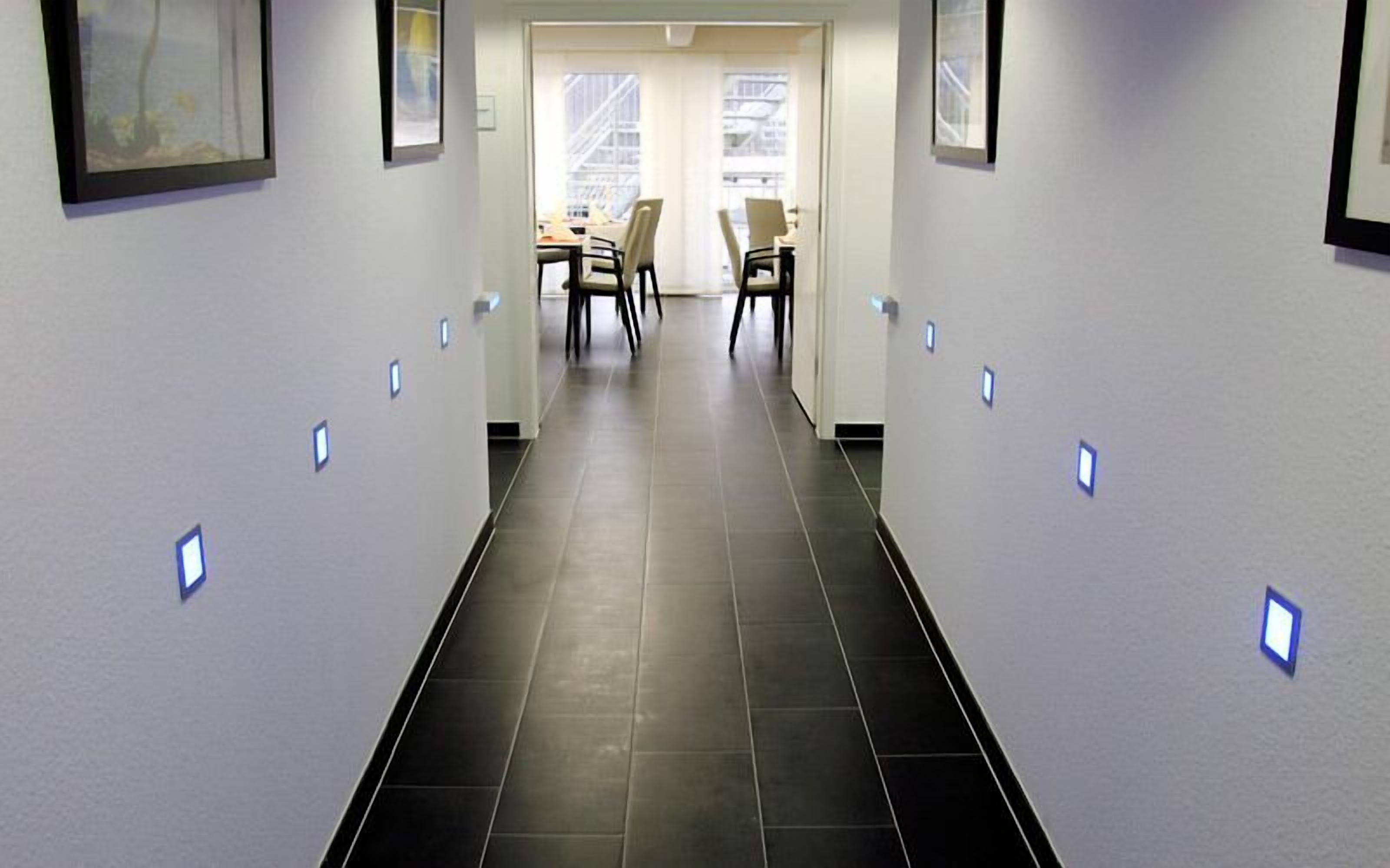 A hallway with a tiled floor, framed pictures on the walls, and a table with chairs in the background.