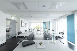 Una sala de conferencias moderna con mesas blancas, sillas negras y un ordenador portátil sobre una mesa.