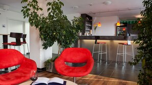 Un intérieur moderne avec des chaises rouges, une table à manger sur laquelle est posé un livre ouvert et un verre à vin, un coin bar et des plantes en pot.