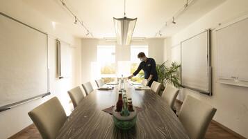 Une salle de conférence avec une longue table, des chaises, un tableau blanc et une plante.