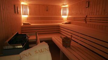 A sauna with wooden benches and benches, a bucket, and a towel with "UNA SAUNA" text.