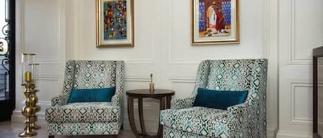 Two patterned armchairs with blue cushions, a small round table, and two framed artworks on the wall.