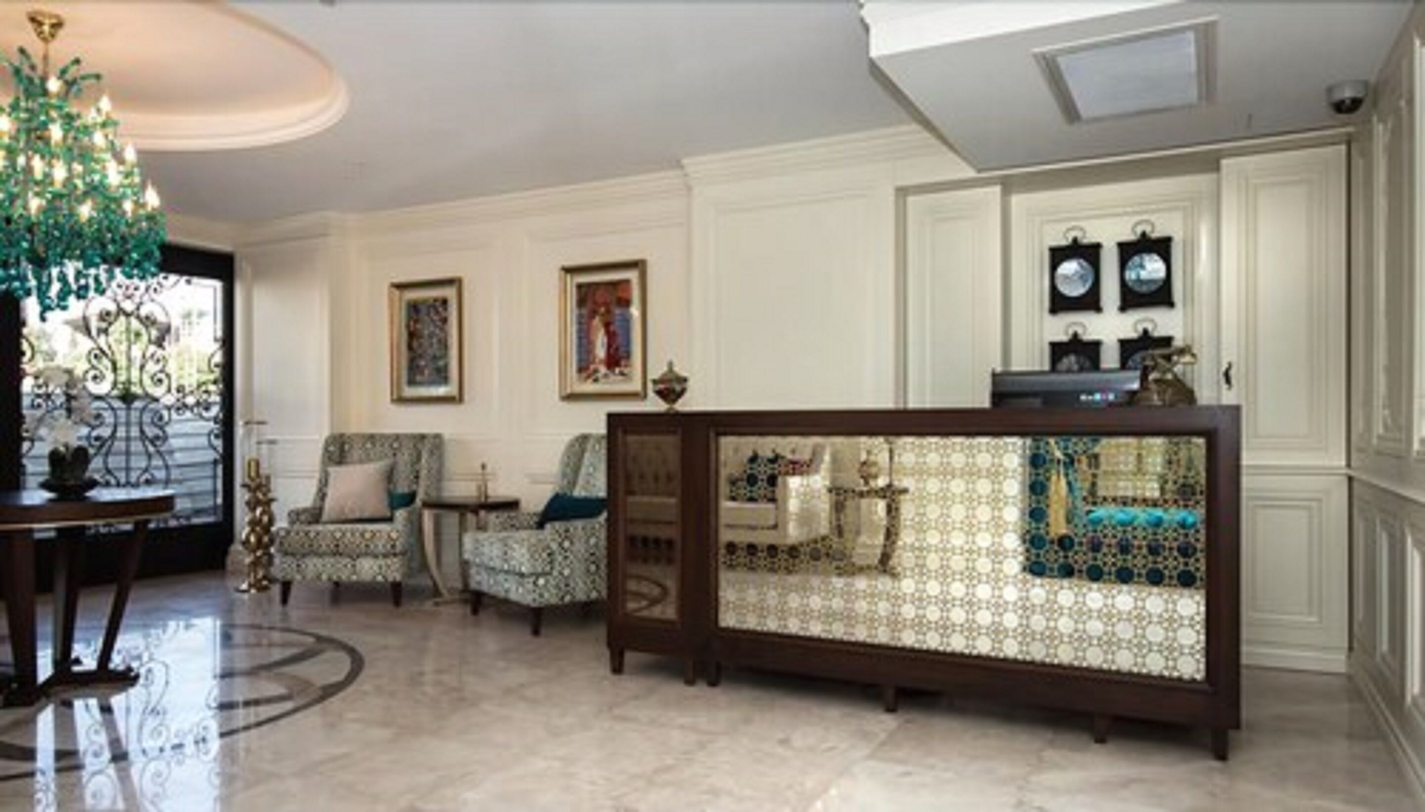 A spacious living room with a marble floor, a decorative console table, two patterned armchairs, and a chandelier.