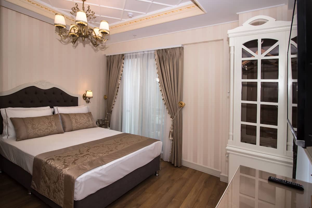 A hotel room with a large bed, a chandelier, curtains, and a wardrobe.