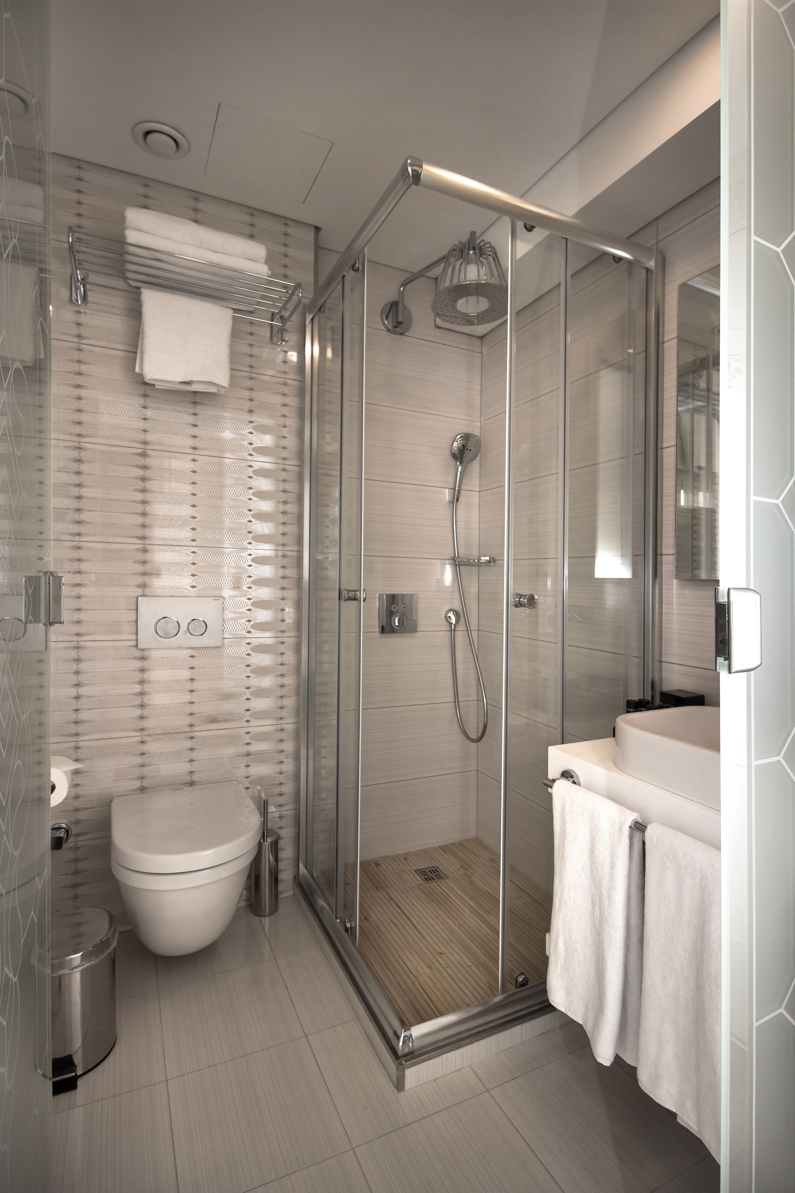 A modern bathroom with a glass-enclosed shower, a toilet, and a sink with a towel rack.