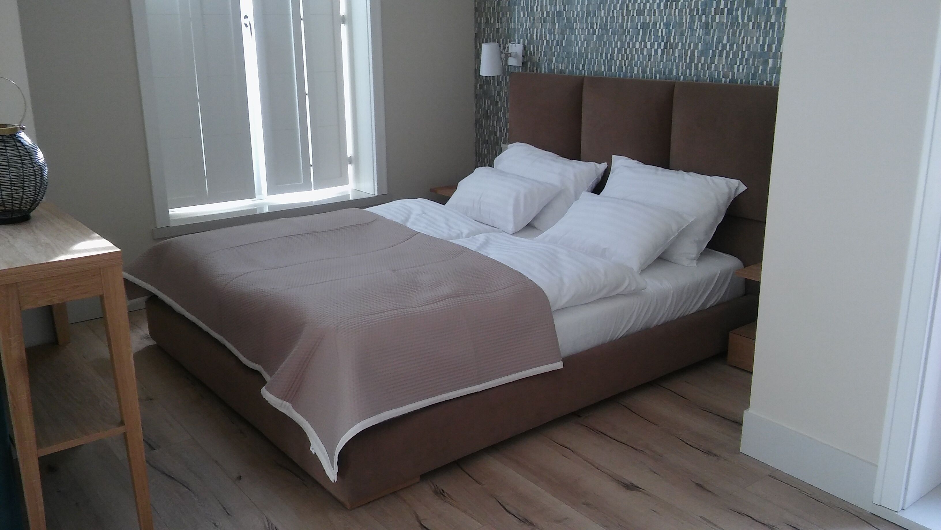 A modern bedroom with a bed, a bedside table, and a window with blinds.