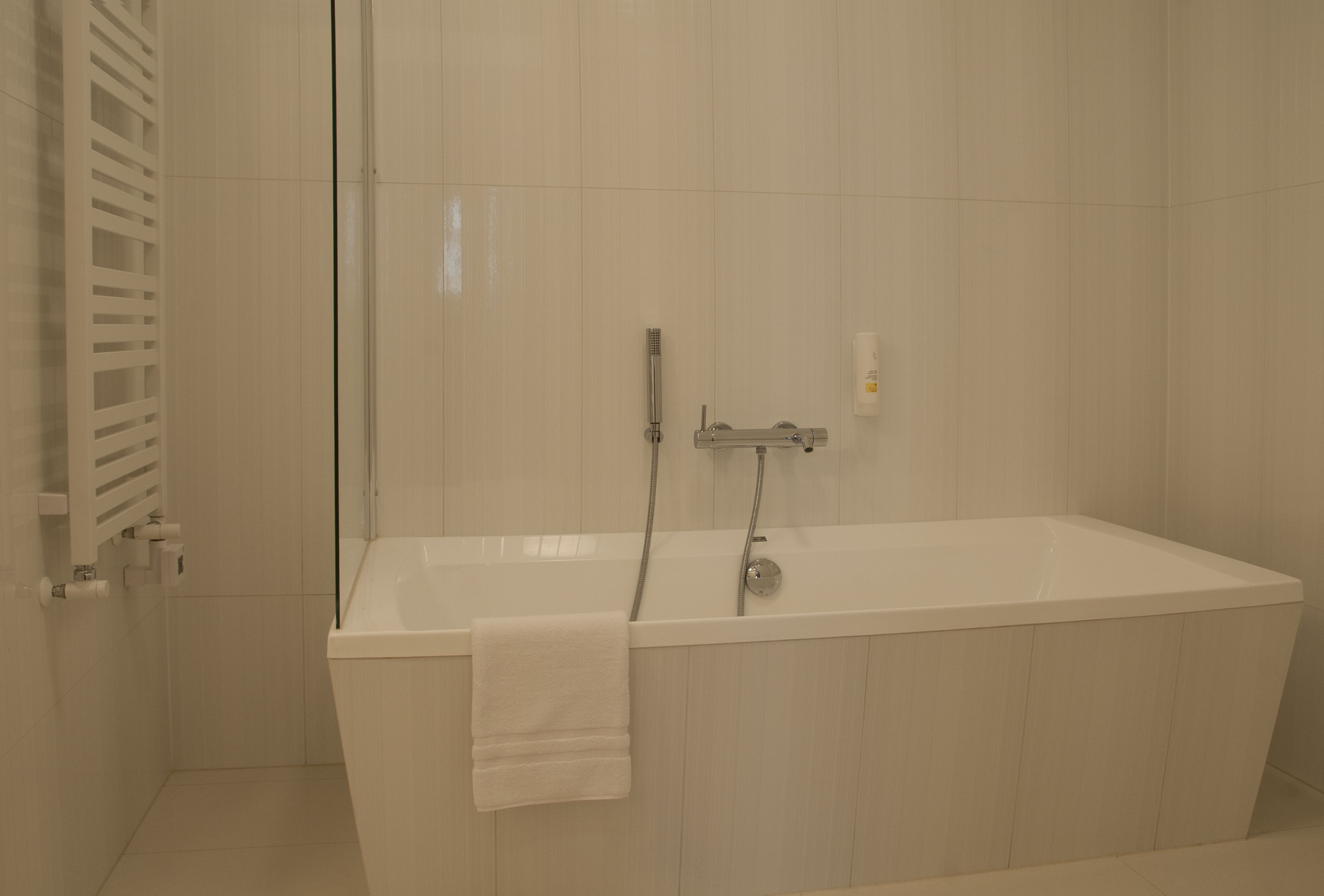 Un baño moderno con una bañera blanca, un cabezal de ducha y un perchero para toallas.